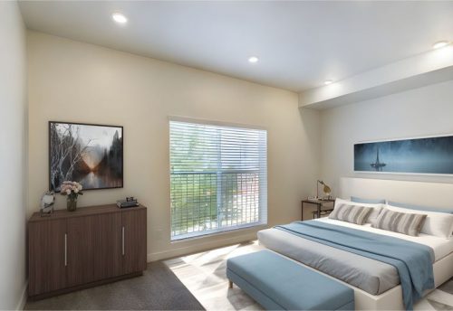 A modern bedroom with a large window, double bed with blue and white bedding, a wooden dresser, wall art, and a bench at the bed’s foot.