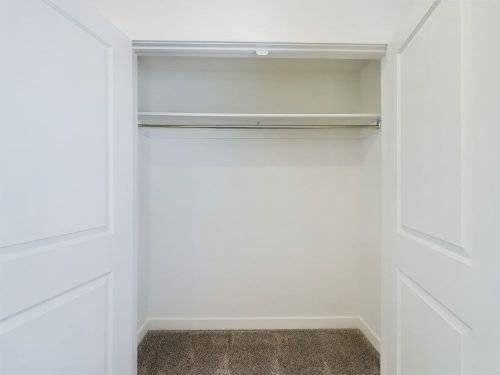 Empty white closet with open double doors, a single metal hanging rod, and carpeted flooring.