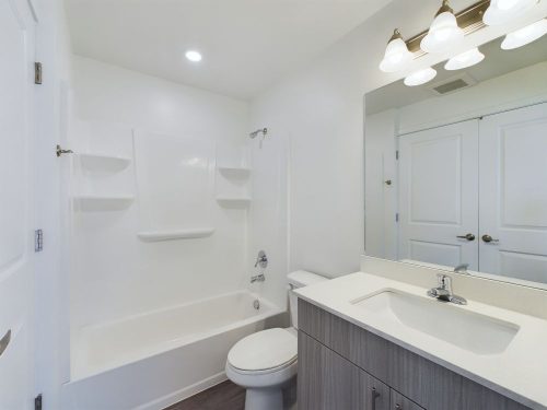 Modern bathroom with white walls, a combined bathtub and shower, toilet, large mirror, vanity with sink, and overhead lighting.